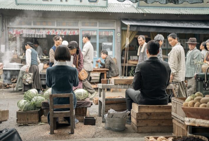 The protagonists Ae-sun and Gwan-sik sitting with their backs to the camera on a bench at the market, in a scene from the Korean series When Life Gives You Tangerines